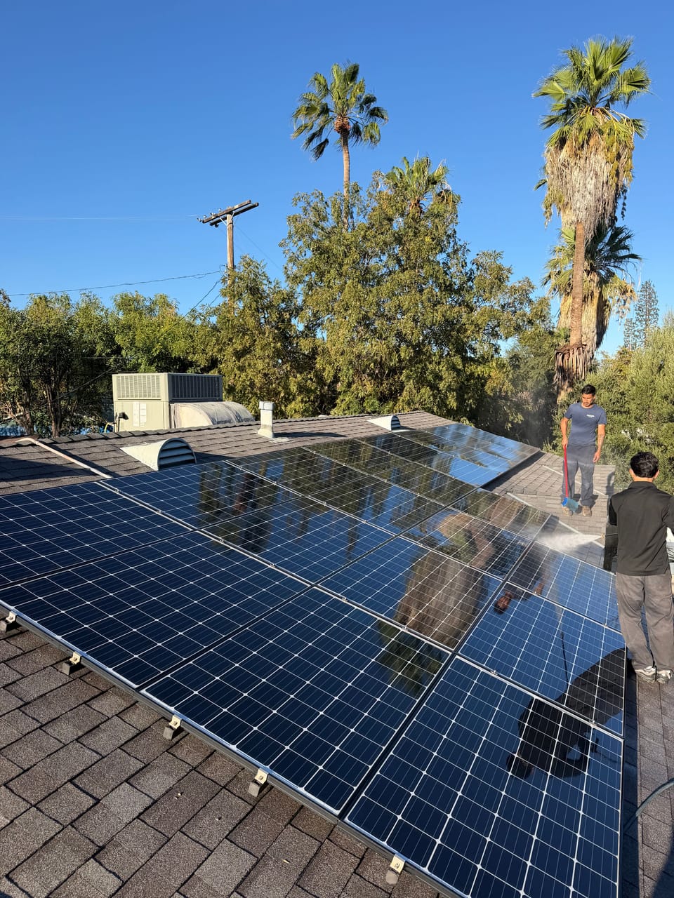 Freshly cleaned solar panel array on a tile roof in North Hills, Los Angeles, with a Salazar Cleaning Services technician at work